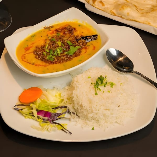 A bowl of yellow dal with spices and cilantro, served with white rice and a side salad.