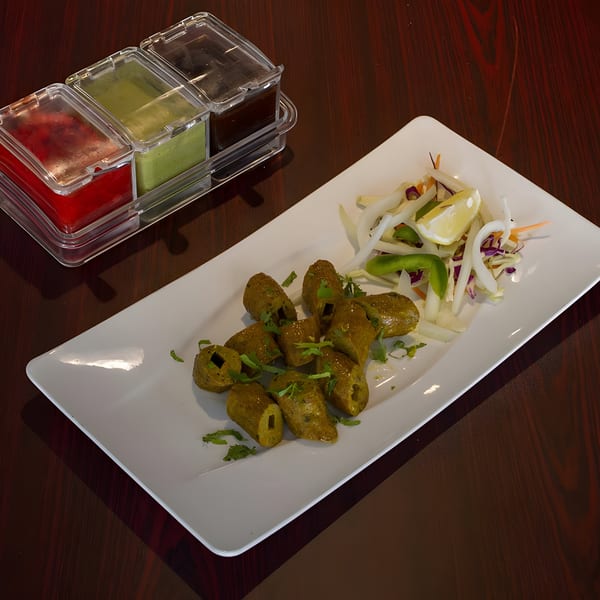 Curry Mantra's green Indian seekh kebabs with salad and three dipping sauces on a white plate.