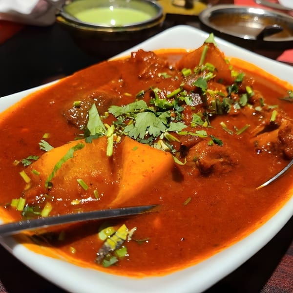 A close-up of a vibrant red Indian curry with potatoes and cilantro in a white dish.
