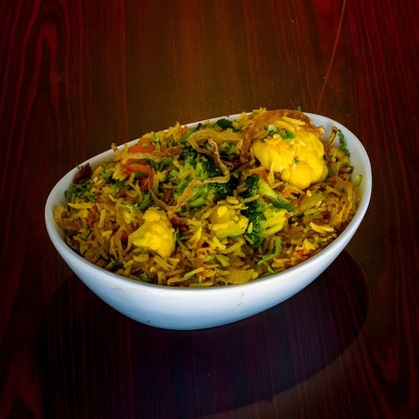 Vegetable Biryani with rice, broccoli, cauliflower, and fried onions in a white bowl.