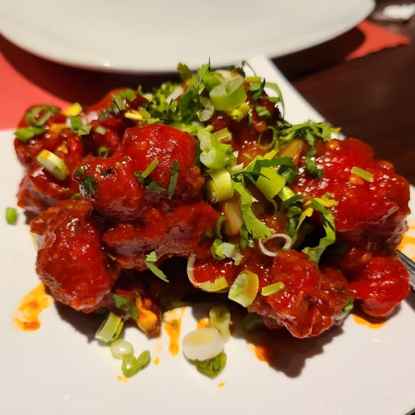 Close-up of bright red Indian chili chicken, garnished with fresh green onions and cilantro.